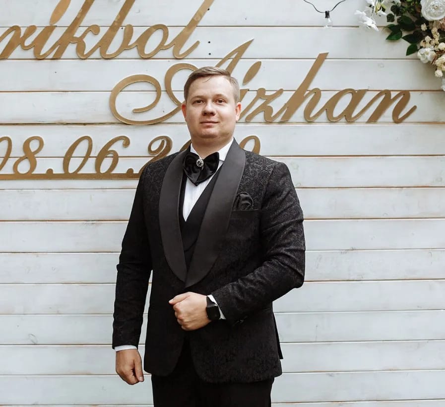 Михаил Архипов, ведущий и тамада, в чёрном смокинге с бабочкой у свадебной фотозоны